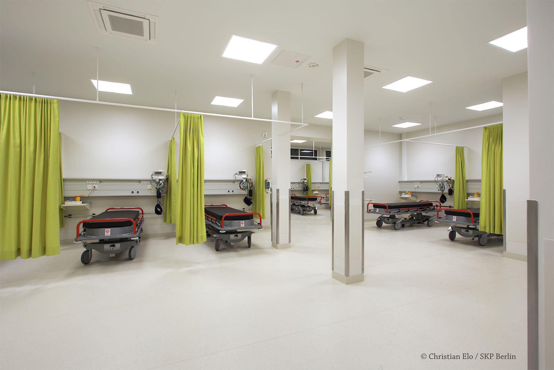 Ein Krankenhauszimmer mit vielen Betten und grünen Vorhängen