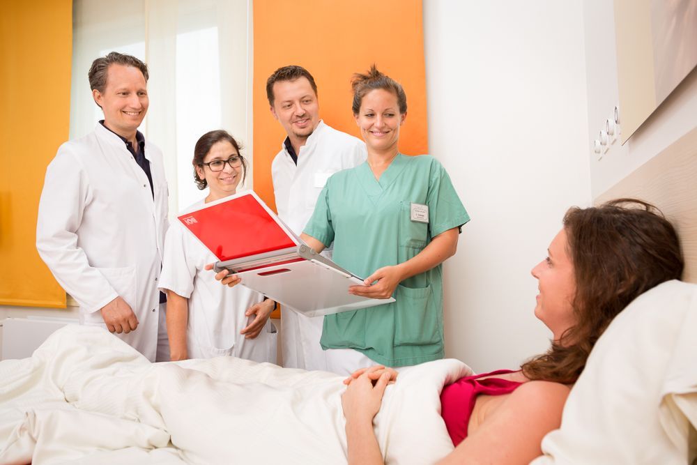 Eine Gruppe von Ärzten und Krankenschwestern steht um eine schwangere Frau in einem Krankenhausbett herum.