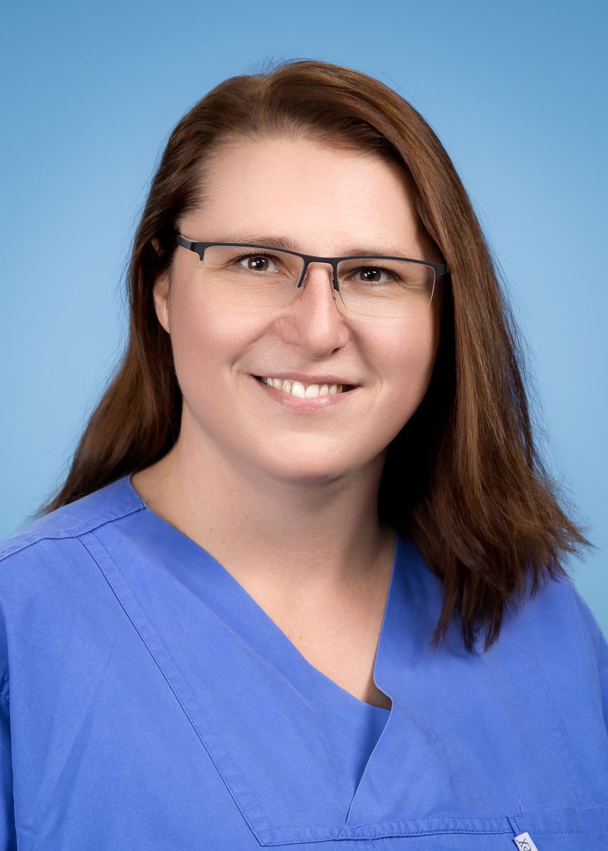 Eine Frau mit Brille und blauem Kasack lächelt in die Kamera.