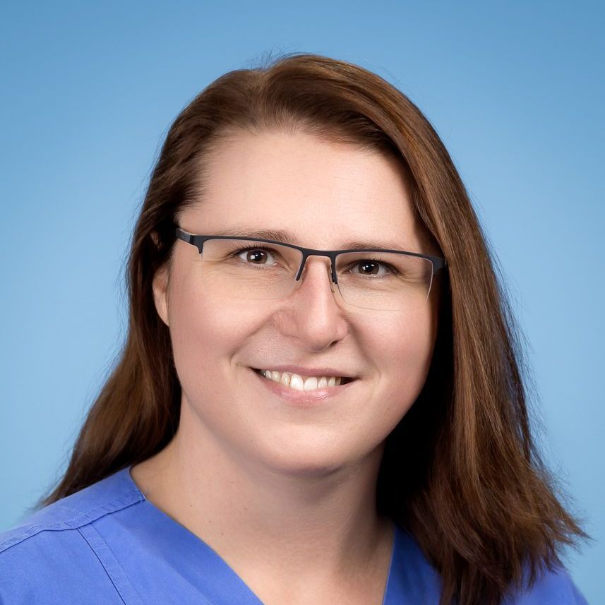 Eine Frau mit Brille und blauem Kasack lächelt in die Kamera.