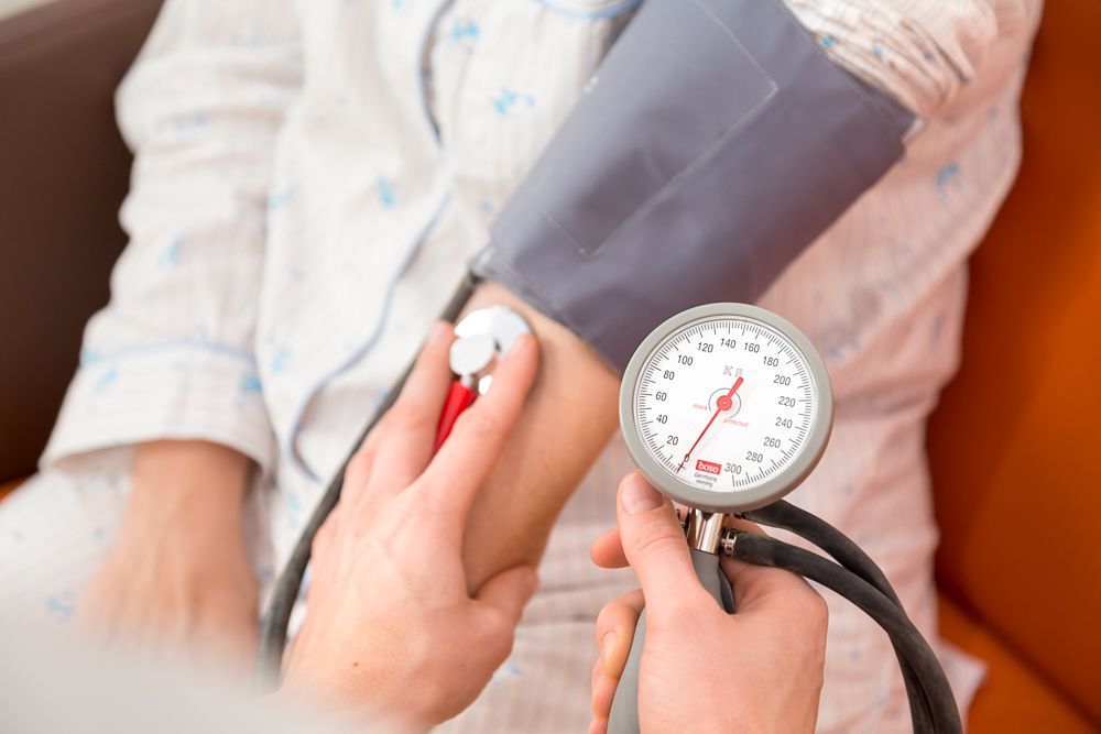Der Blutdruck am Arm einer Person mit angelegter Blutdruckmanschette wird mit einem manuellen Messgerät abgelesen.