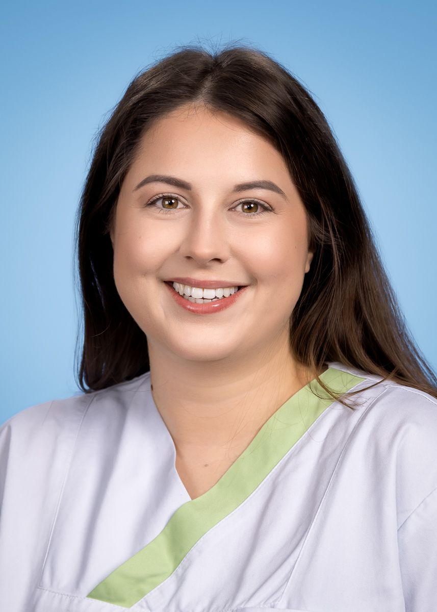 Eine Frau im weißen Kittel lächelt in die Kamera.