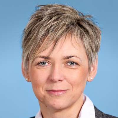 Eine Nahaufnahme des Gesichts einer Frau mit kurzen Haaren und blauem Hintergrund.