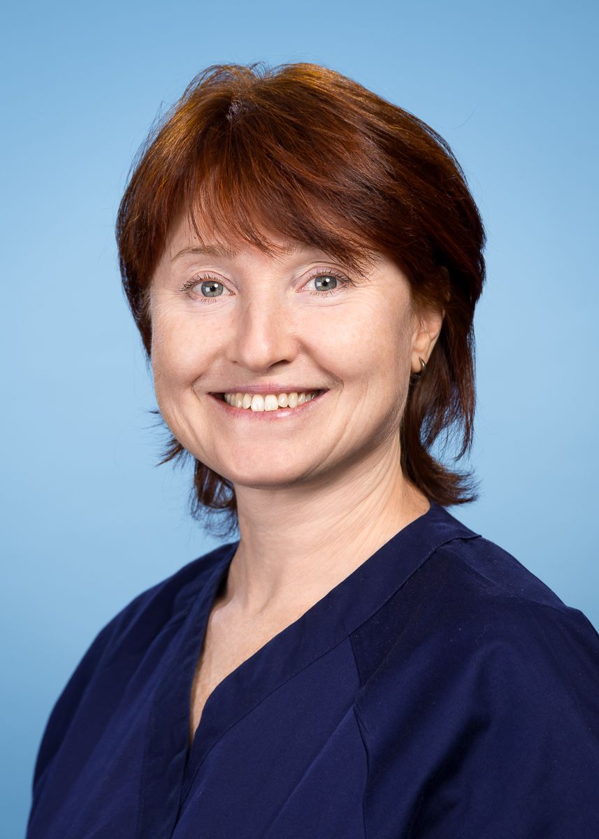 Eine Frau mit kurzen Haaren und einer Tätowierung auf der Brust lächelt in die Kamera.