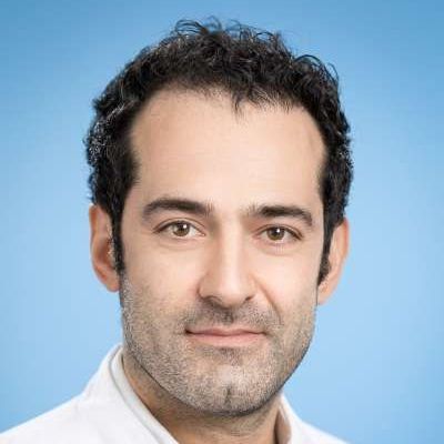 Ein Mann mit lockigem Haar und Bart lächelt in die Kamera.