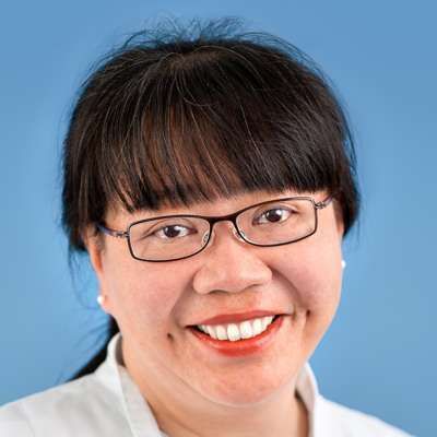 Eine Frau mit Brille und weißem Hemd lächelt in die Kamera.