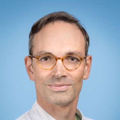 Ein Mann mit Brille und weißem Hemd lächelt in die Kamera.