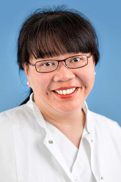 Eine Frau mit Brille und weißem Kittel lächelt in die Kamera.