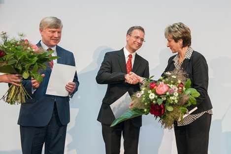 Ein Mann im Anzug schüttelt einer Frau, die einen Blumenstrauß hält, die Hand.