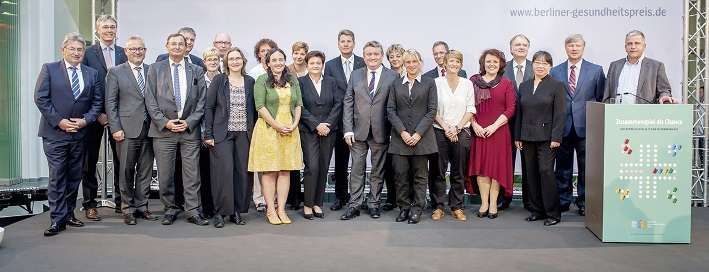 Eine große Gruppe von Menschen posiert vor einem Podium für ein Foto.
