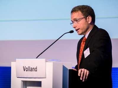 Ein Mann in Anzug und Krawatte steht an einem Podium und hält eine Rede.