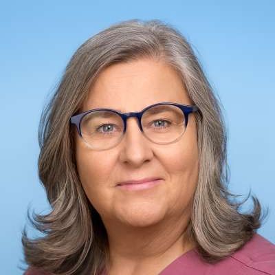 Eine Frau mit Brille und rosa Kasack lächelt in die Kamera.