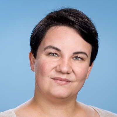 Eine Frau mit kurzen Haaren und einer Tätowierung auf der Brust lächelt in die Kamera.