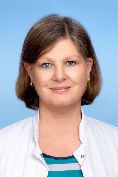 Eine Frau in einem weißen Kittel und einem gestreiften Hemd lächelt in die Kamera.