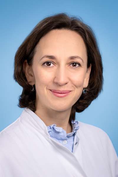 Eine Frau im weißen Kittel lächelt in die Kamera.