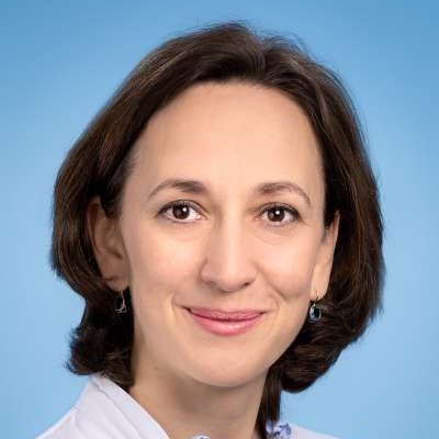 Eine Frau mit Ohrringen und weißem Hemd lächelt in die Kamera.