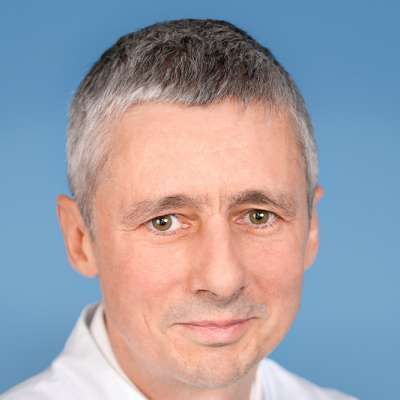 Ein Mann mit grauem Haar trägt ein weißes Hemd und lächelt in die Kamera.