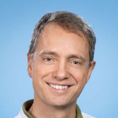 Ein Mann in einem weißen Hemd und einem grünen Kragen lächelt in die Kamera.