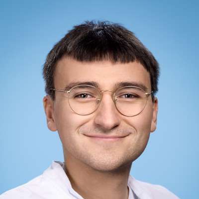 Ein junger Mann mit Brille und weißem Hemd lächelt in die Kamera.