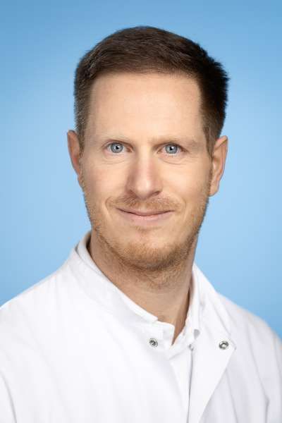 Ein Mann im weißen Laborkittel lächelt in die Kamera.