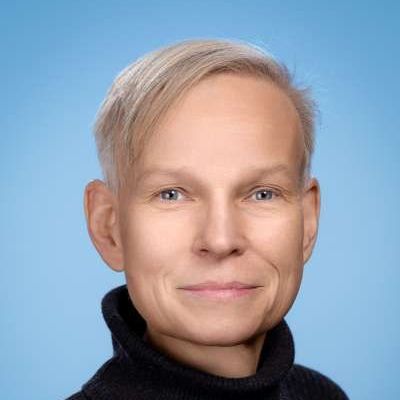 Ein Mann mit blondem Haar trägt einen schwarzen Rollkragenpullover und lächelt in die Kamera.