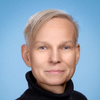 Ein Mann mit blondem Haar trägt einen schwarzen Rollkragenpullover und lächelt in die Kamera.