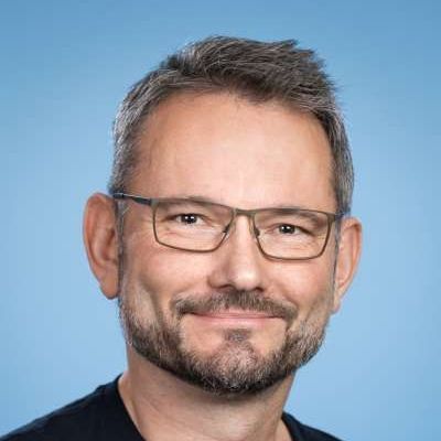 Ein Mann mit Bart und Brille lächelt in die Kamera.