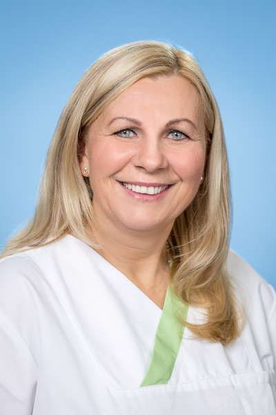 Eine Frau im weißen Kittel lächelt in die Kamera.