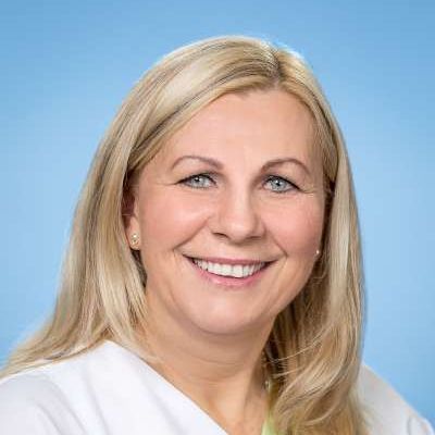 Eine Frau im weißen Kittel lächelt in die Kamera.