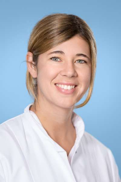 Eine Frau im weißen Laborkittel lächelt in die Kamera