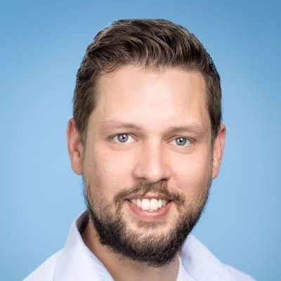 Ein Mann mit Bart und einem weißen Hemd lächelt in die Kamera.