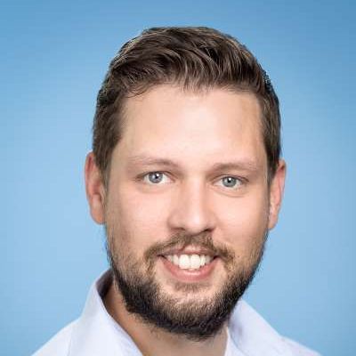 Ein Mann mit Bart und einem weißen Hemd lächelt in die Kamera.