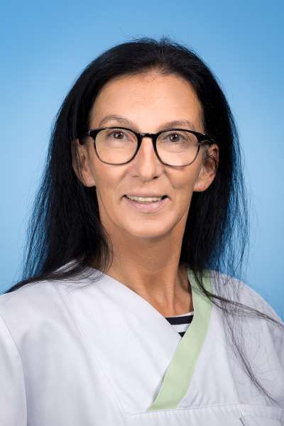 Eine Frau mit Brille und weißem Kittel lächelt in die Kamera.