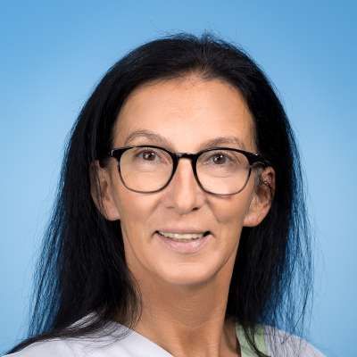 Eine Frau mit Brille und weißem Hemd lächelt in die Kamera.