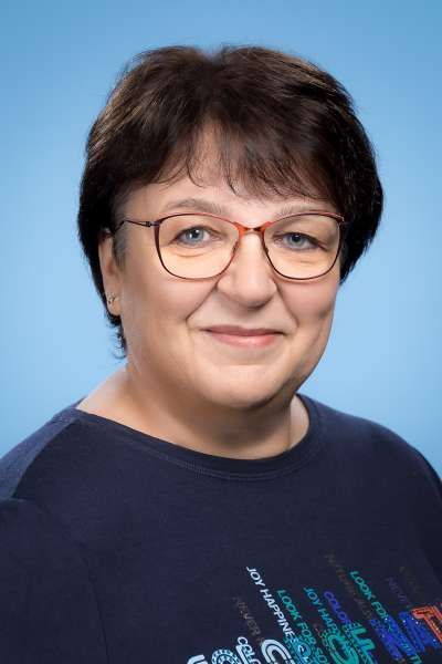 Eine Frau mit Brille und blauem Hemd lächelt in die Kamera.