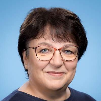 Eine Frau mit Brille und blauem Hemd lächelt in die Kamera.