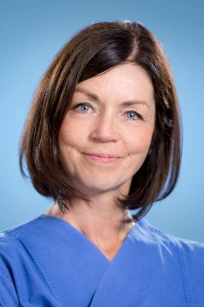 Eine Frau in einem blauen Kasack lächelt in die Kamera.