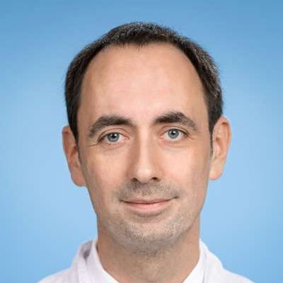 Ein Mann in weißem Hemd und Krawatte lächelt in die Kamera.