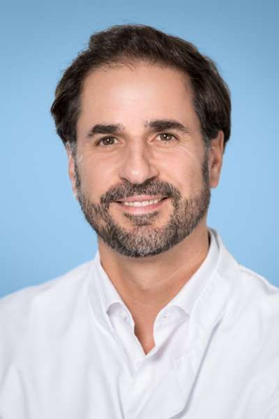 Ein Mann mit Bart trägt ein weißes Hemd und lächelt in die Kamera.