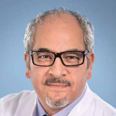 Ein Mann mit Brille und Bart trägt einen weißen Mantel und eine Krawatte.