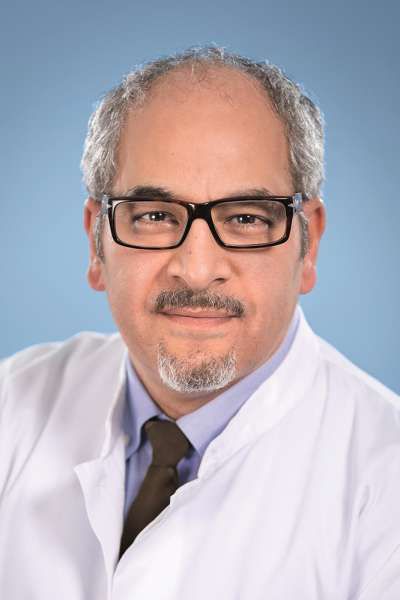 Ein Mann mit Brille und Bart trägt einen weißen Mantel und eine Krawatte.