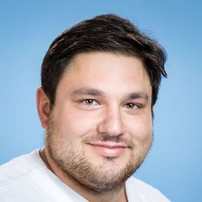 Ein Mann mit Bart und einem weißen Hemd lächelt in die Kamera.