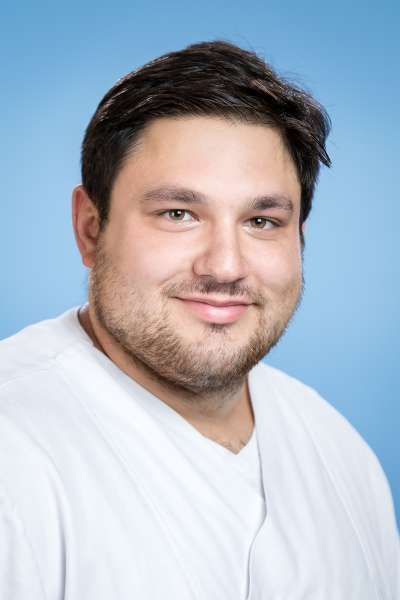 Ein Mann mit Bart trägt ein weißes Hemd und lächelt in die Kamera.