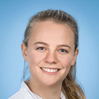 Eine junge Frau lächelt vor einem blauen Hintergrund in die Kamera.