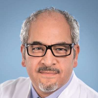 Ein Mann mit Brille und Bart trägt einen weißen Mantel und eine Krawatte.