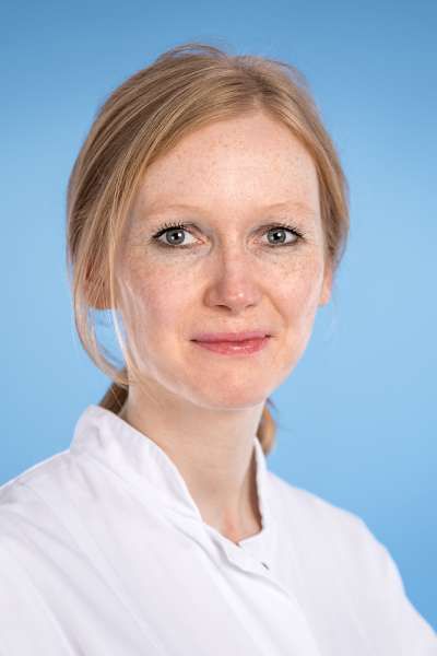 Eine Frau in einem weißen Laborkittel lächelt in die Kamera.