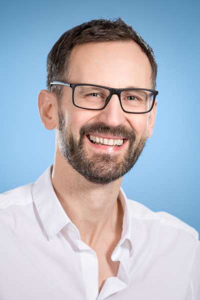 Ein Mann mit Bart und Brille lächelt in die Kamera.