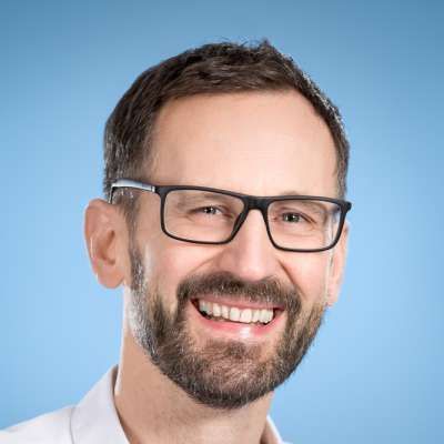 Ein Mann mit Bart und Brille lächelt in die Kamera.