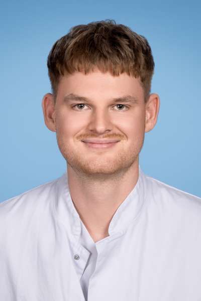 Ein junger Mann im weißen Laborkittel lächelt in die Kamera.