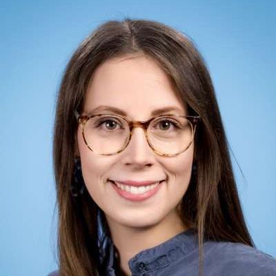 Eine Frau mit Brille und blauem Hemd lächelt in die Kamera.